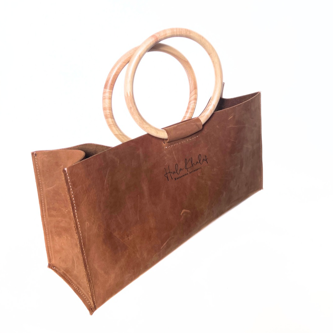 Tan grain leather tote with suede interior and oak wooden handle shown at an angle.