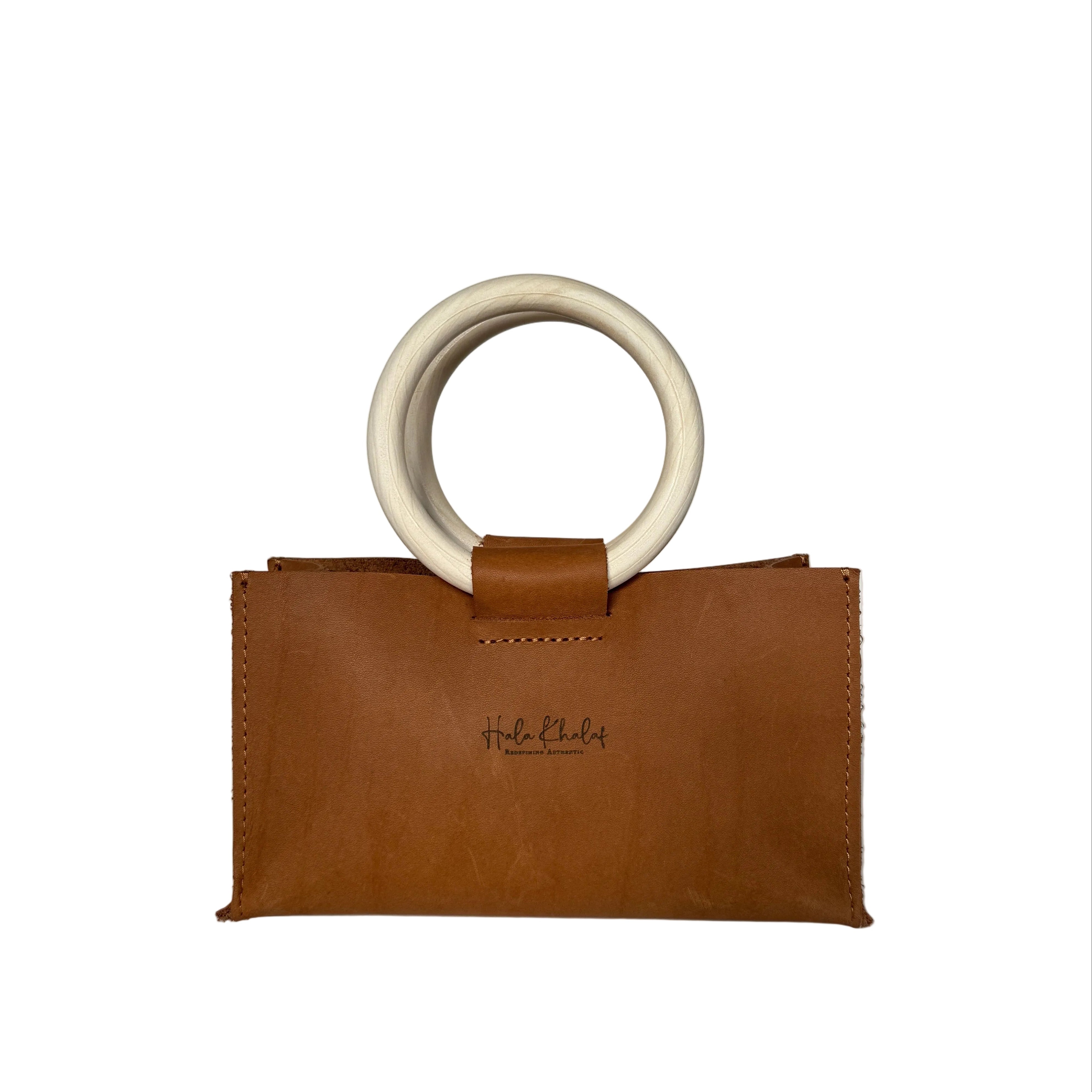 A mini tan leather clutch bag with a circular off-white handle, displayed against a neutral gray background. The brand name 'Held & Held' is printed on the front.